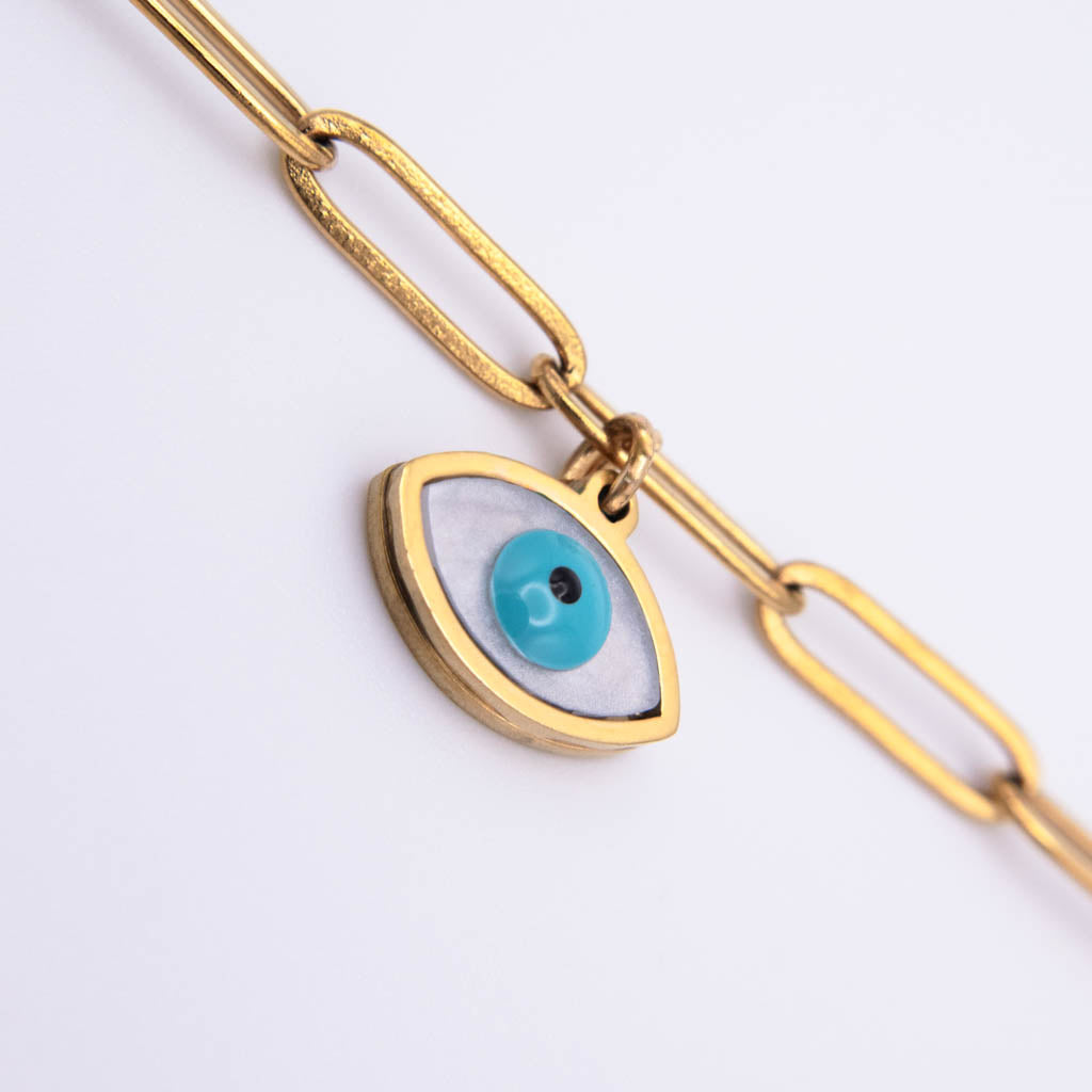 Gold paperclip chain anklet with an evil eye charm featuring a turquoise blue iris and white background, shown on a clean white surface.