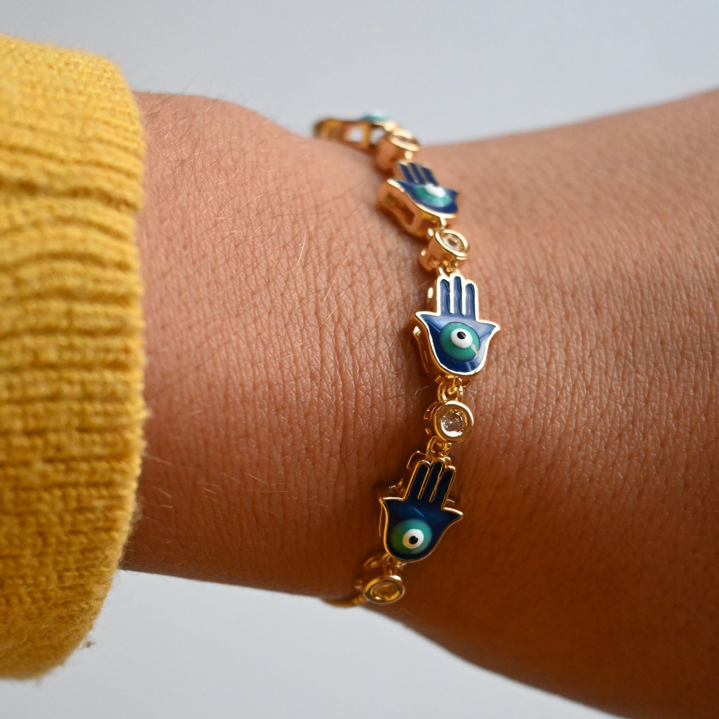 Bracelet with hand and eye charms on a wrist against a neutral background