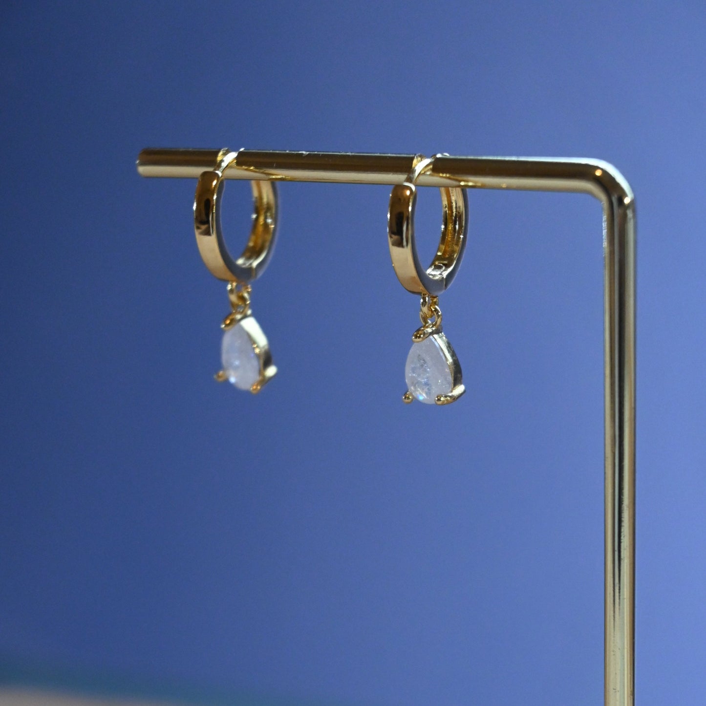 Gold earrings with gemstones on a stand against a blue background
