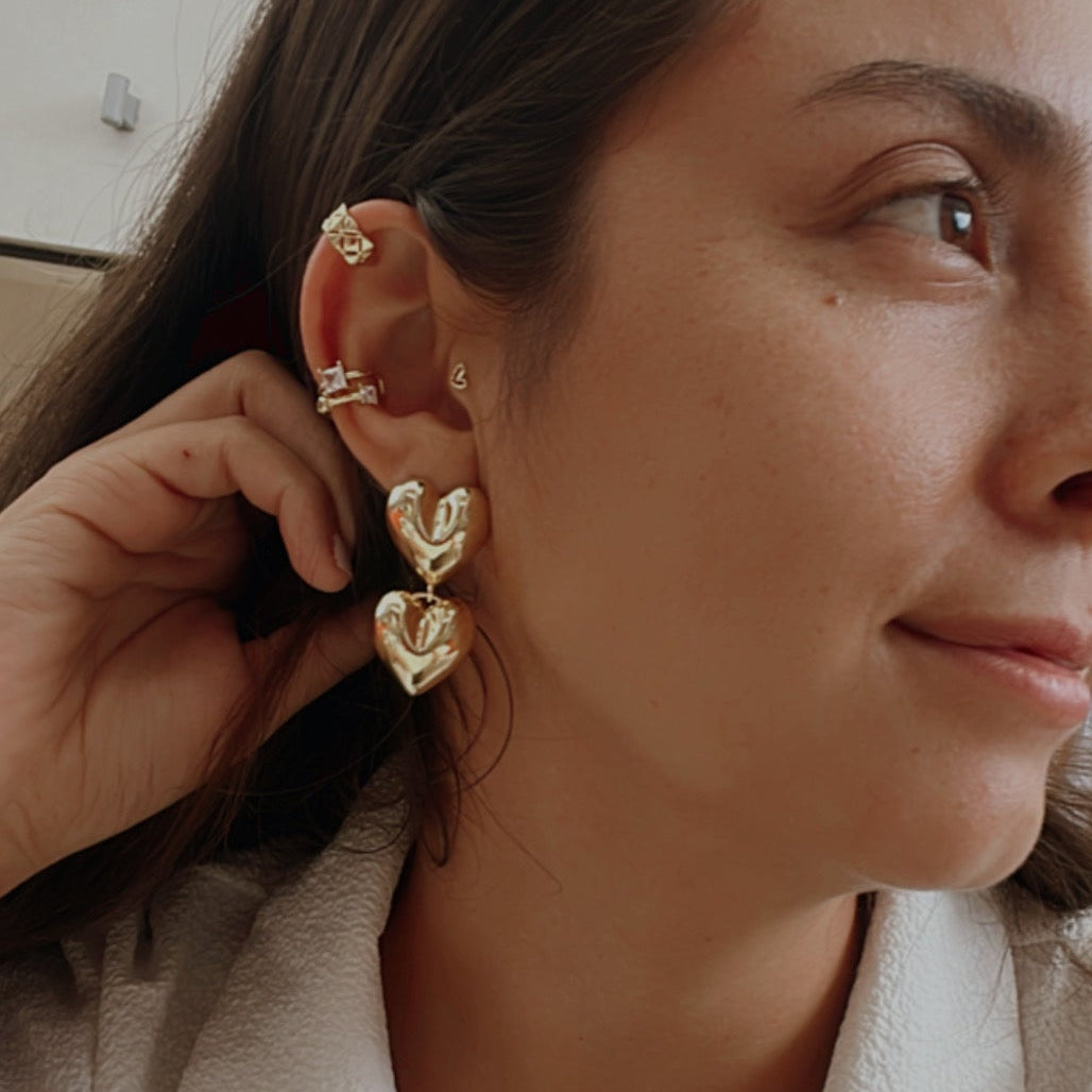 Woman wearing gold heart-shaped earrings and a white shirt.
