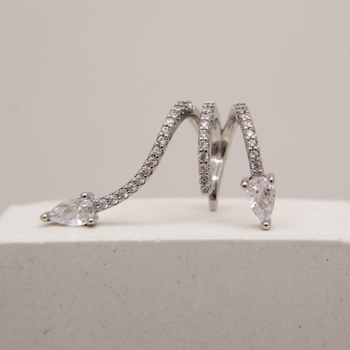 Pair of silver hoop ear cuff with clear gemstones on a light gray background