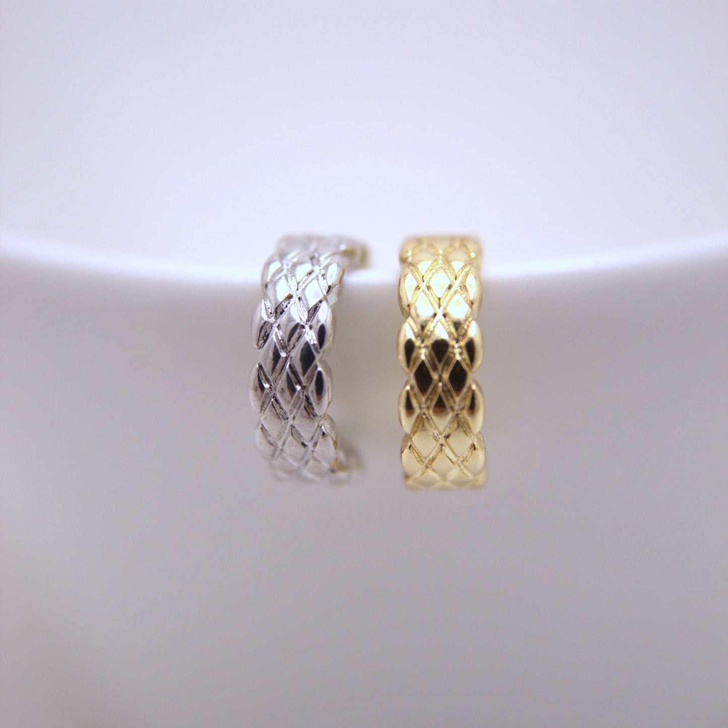 Two woven ear cuffs one silver and one gold, on a white background