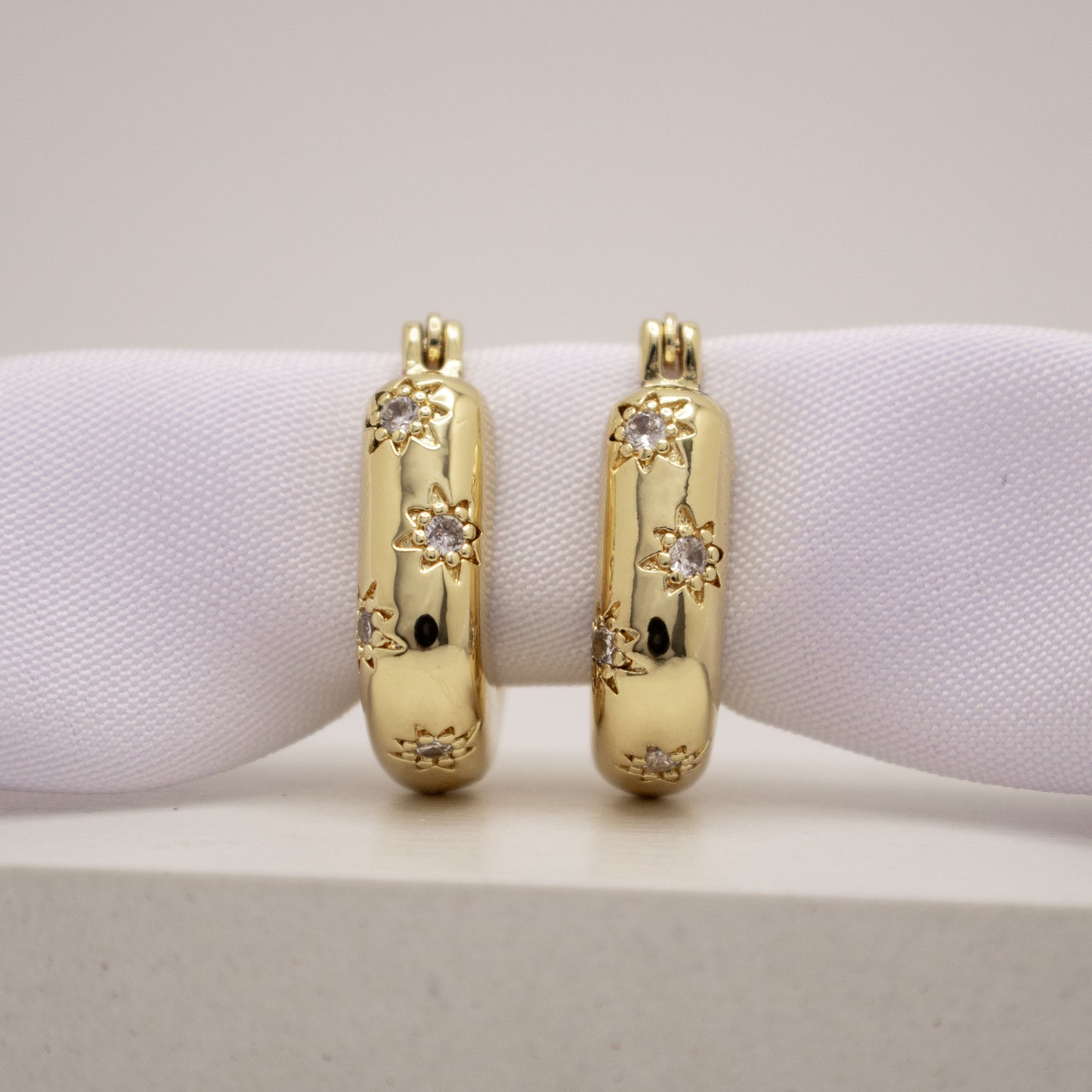 Gold hoop earrings with diamond accents on a white cushion