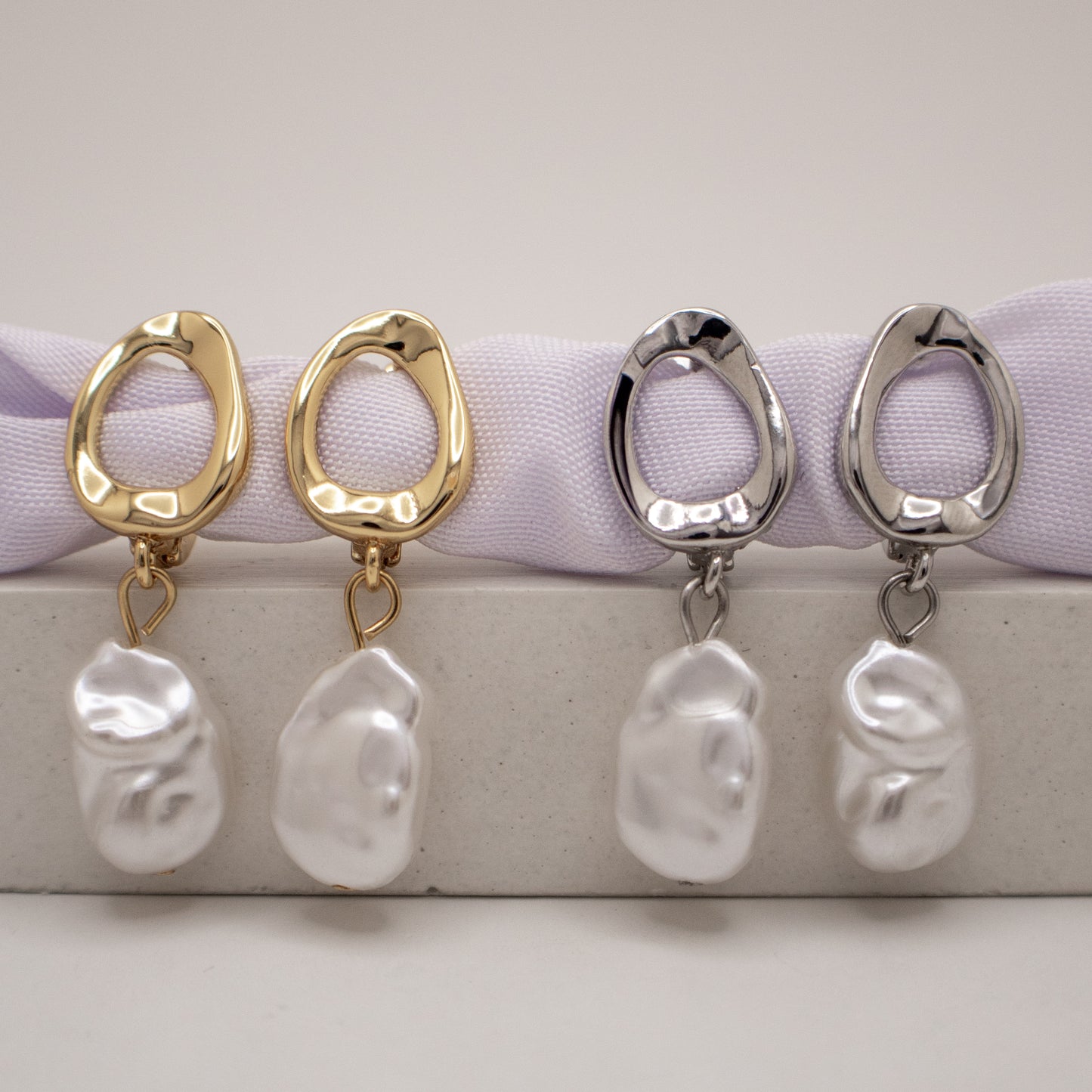 Pair of gold and silver hoop earrings with pearl-like charms on a white background