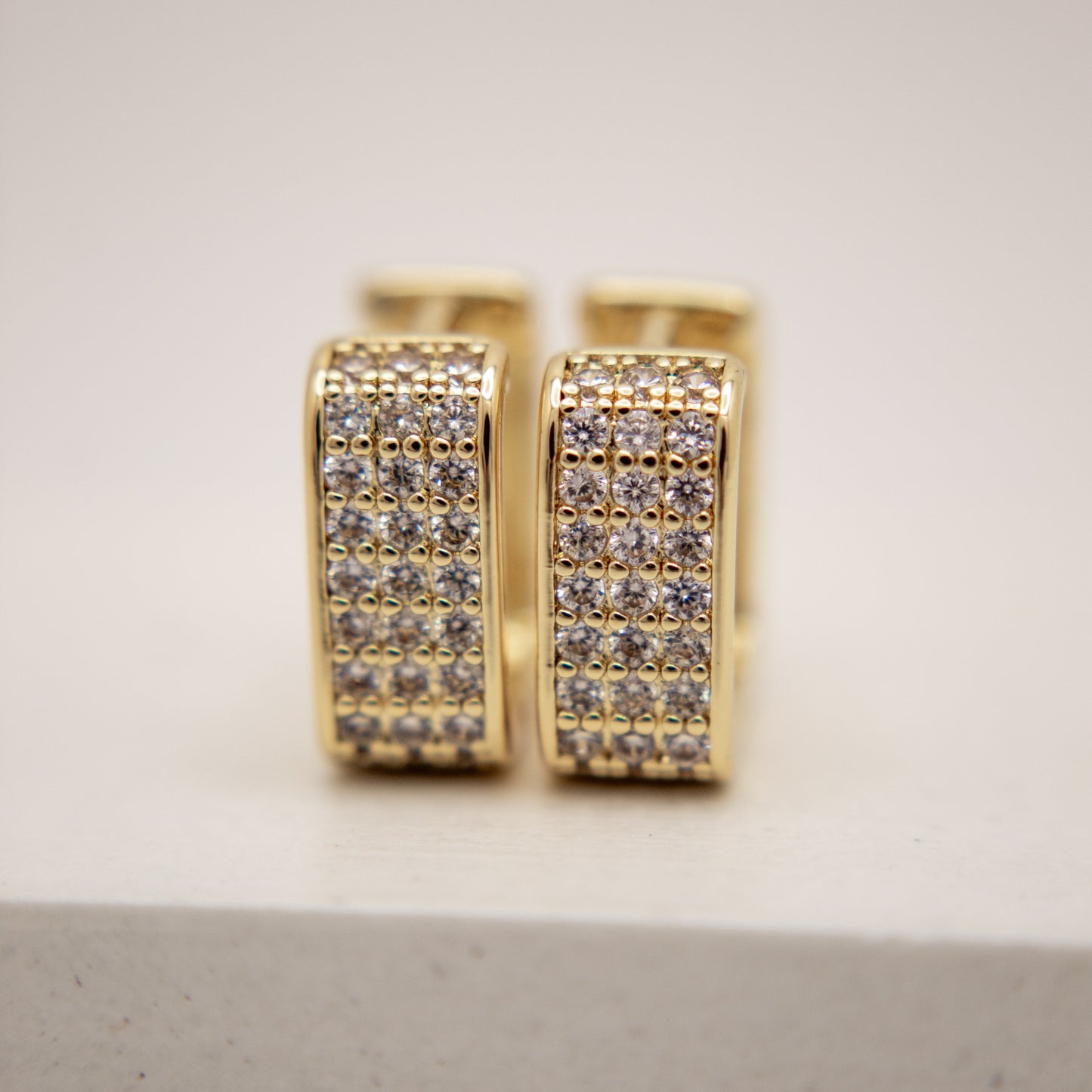 Gold hoop earrings with embedded diamonds on a light gray background