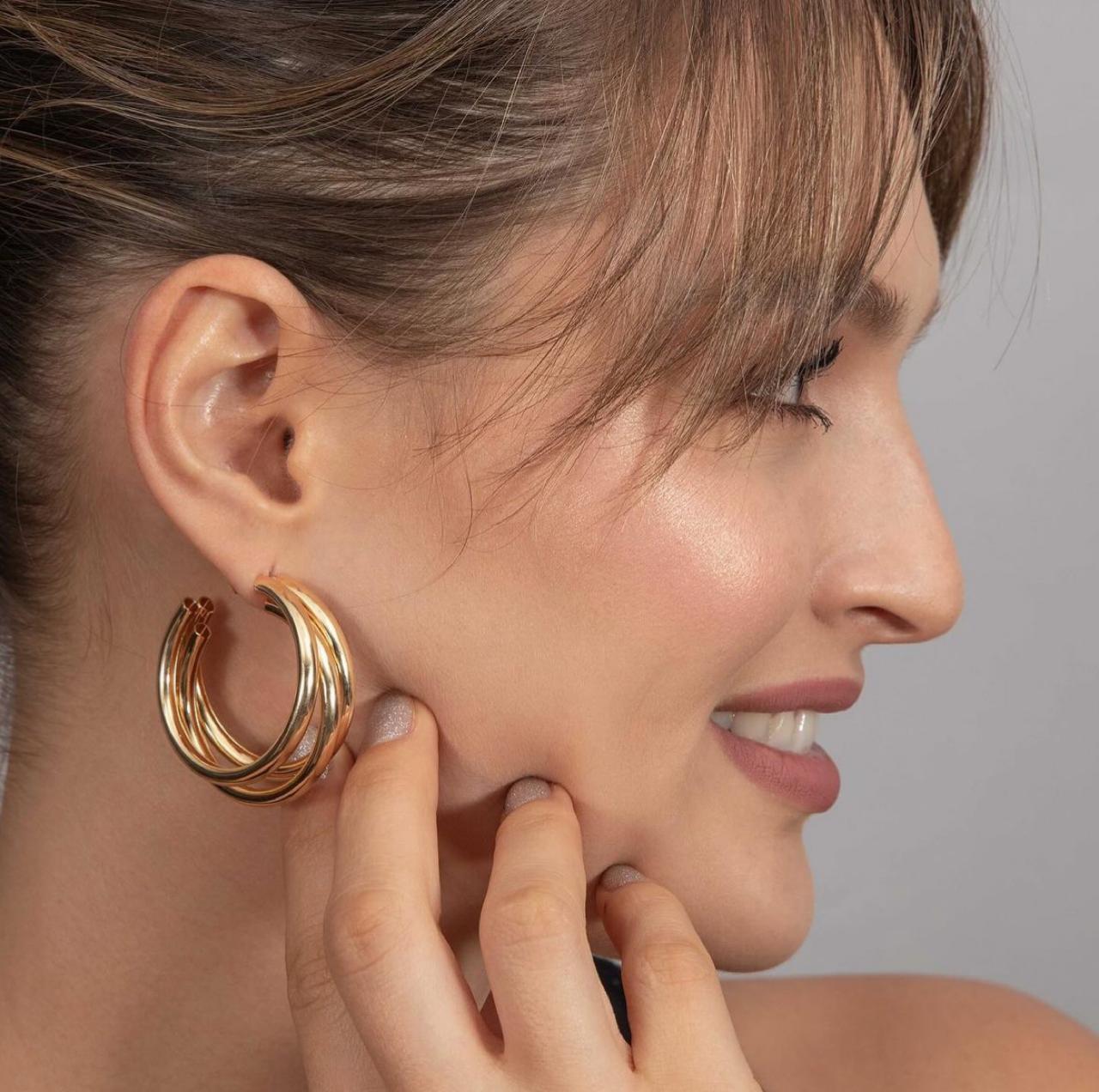 A close-up image of a woman wearing a large gold-plated hoop earring.
