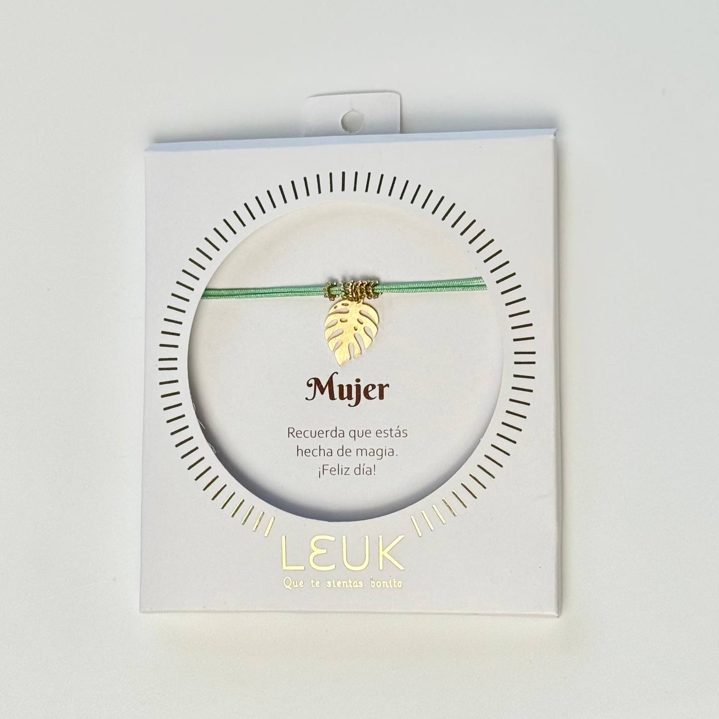 Bracelet with a gold charm in a LEUK branded packaging on a light gray background
