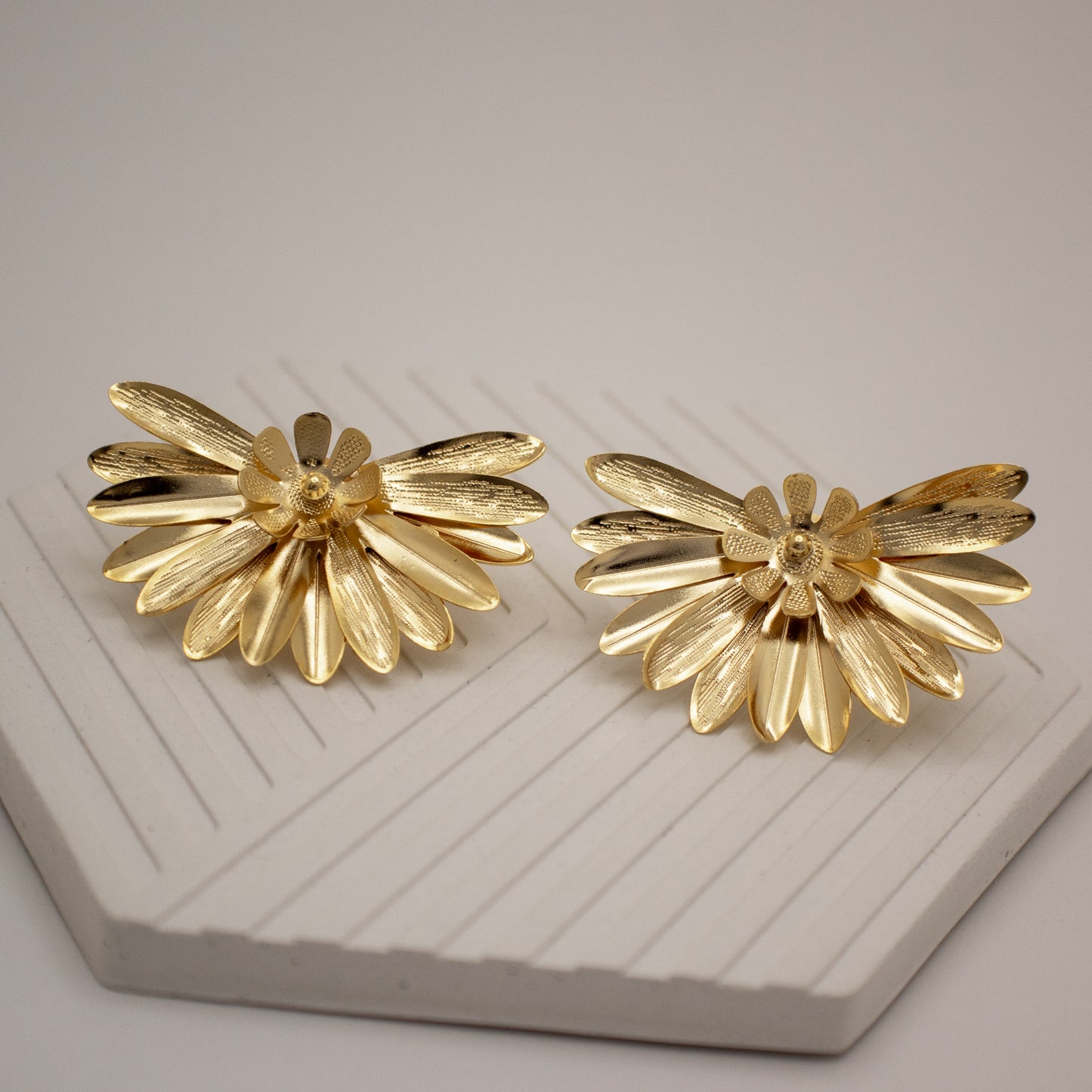 Pair of gold flower-shaped earrings on a textured surface