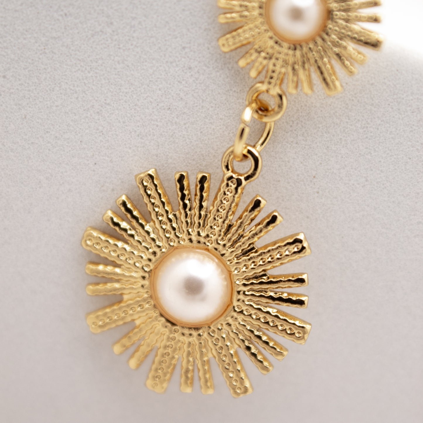 Gold dandelion-shaped earrings with pearl centers on a light gray background