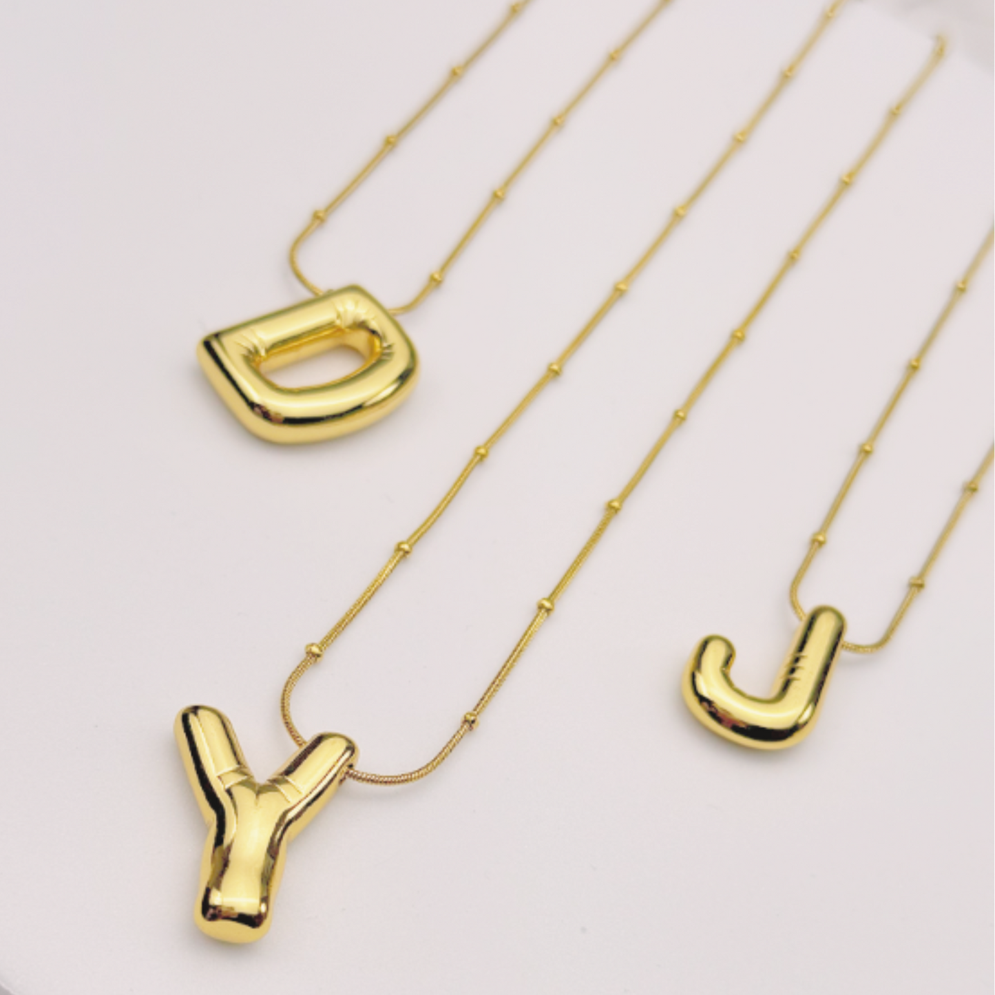 Gold necklaces with letter pendants on a white surface