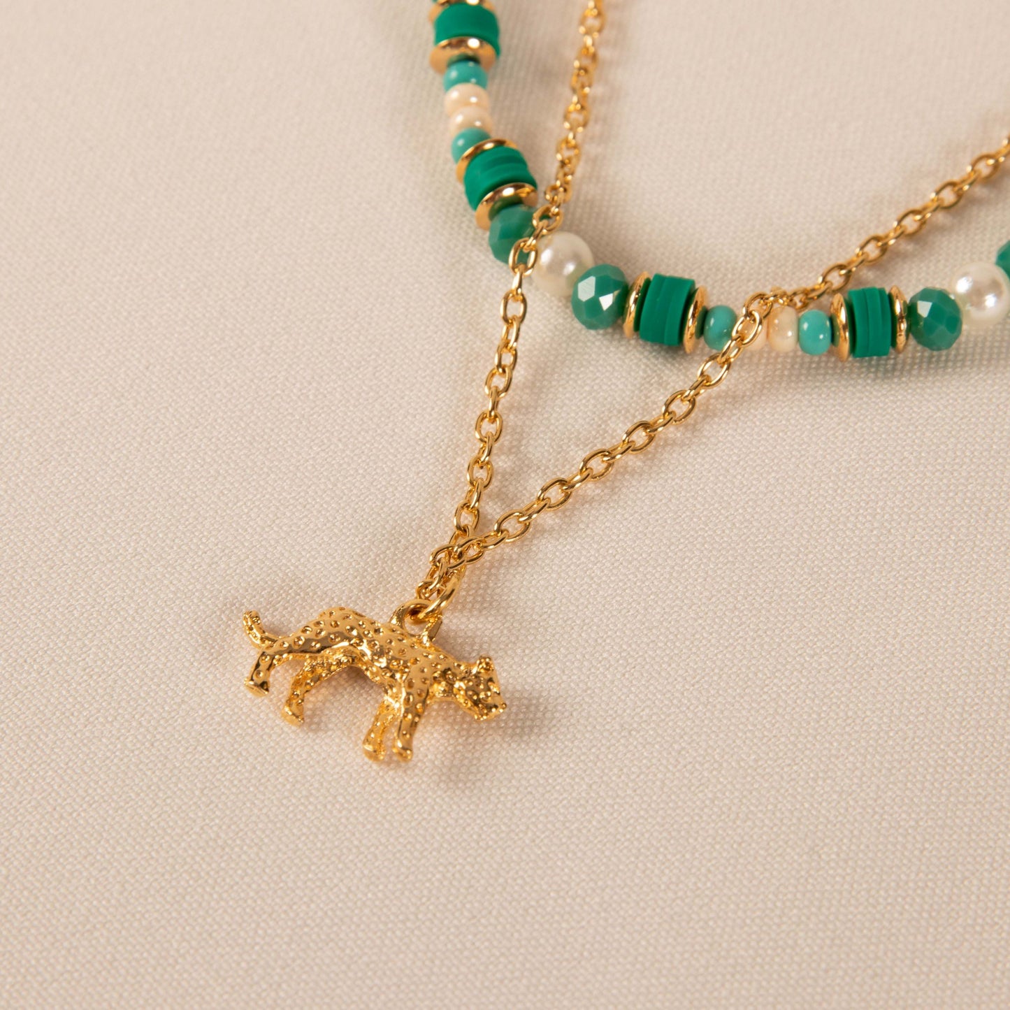Necklace with gold charm and green and white bead details on a beige background