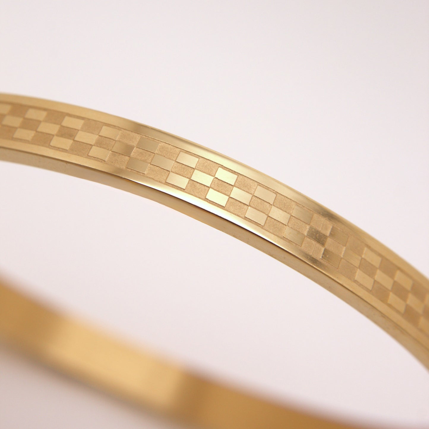 Gold bracelet with a checkered pattern on a light pink background