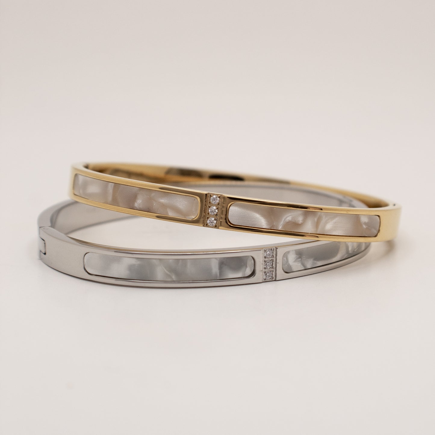 Two bracelets, one gold and one silver, on a light beige background
