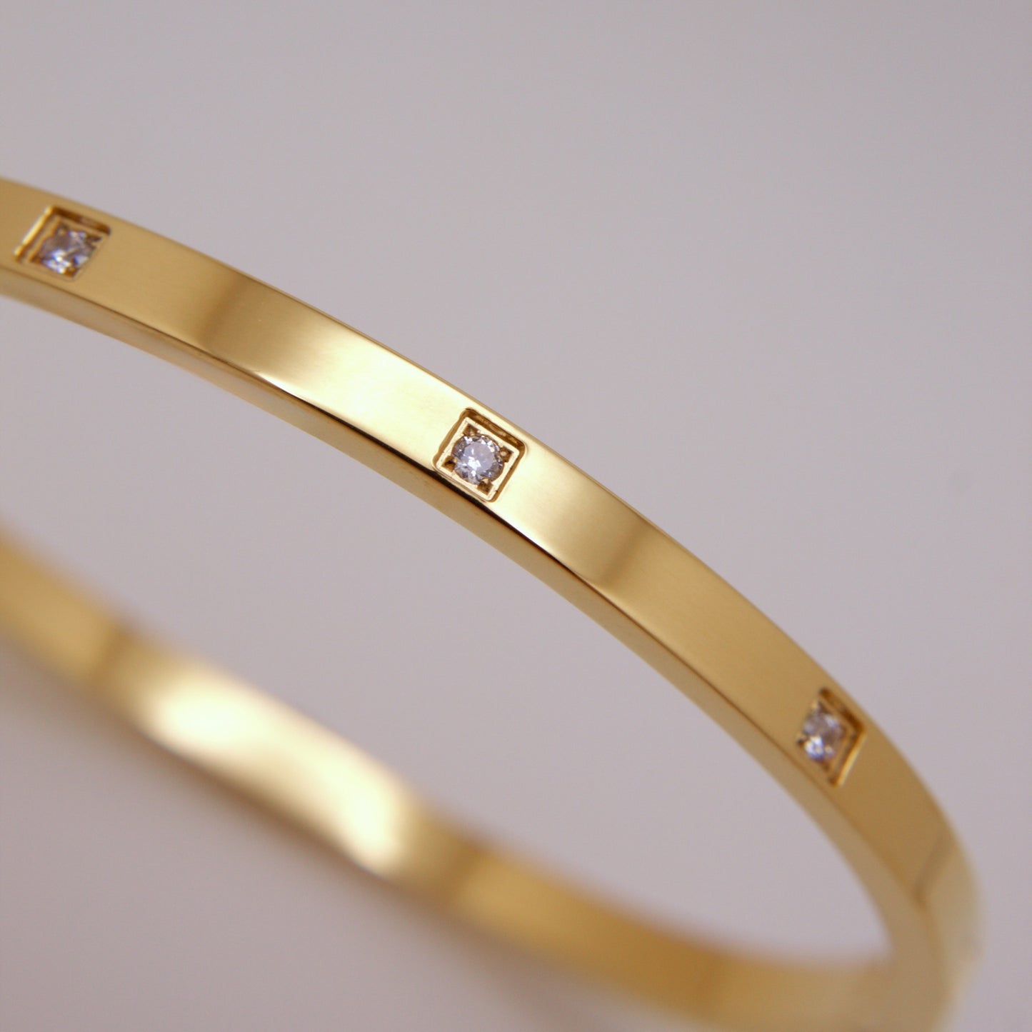Gold bracelet with embedded diamonds on a light gray background