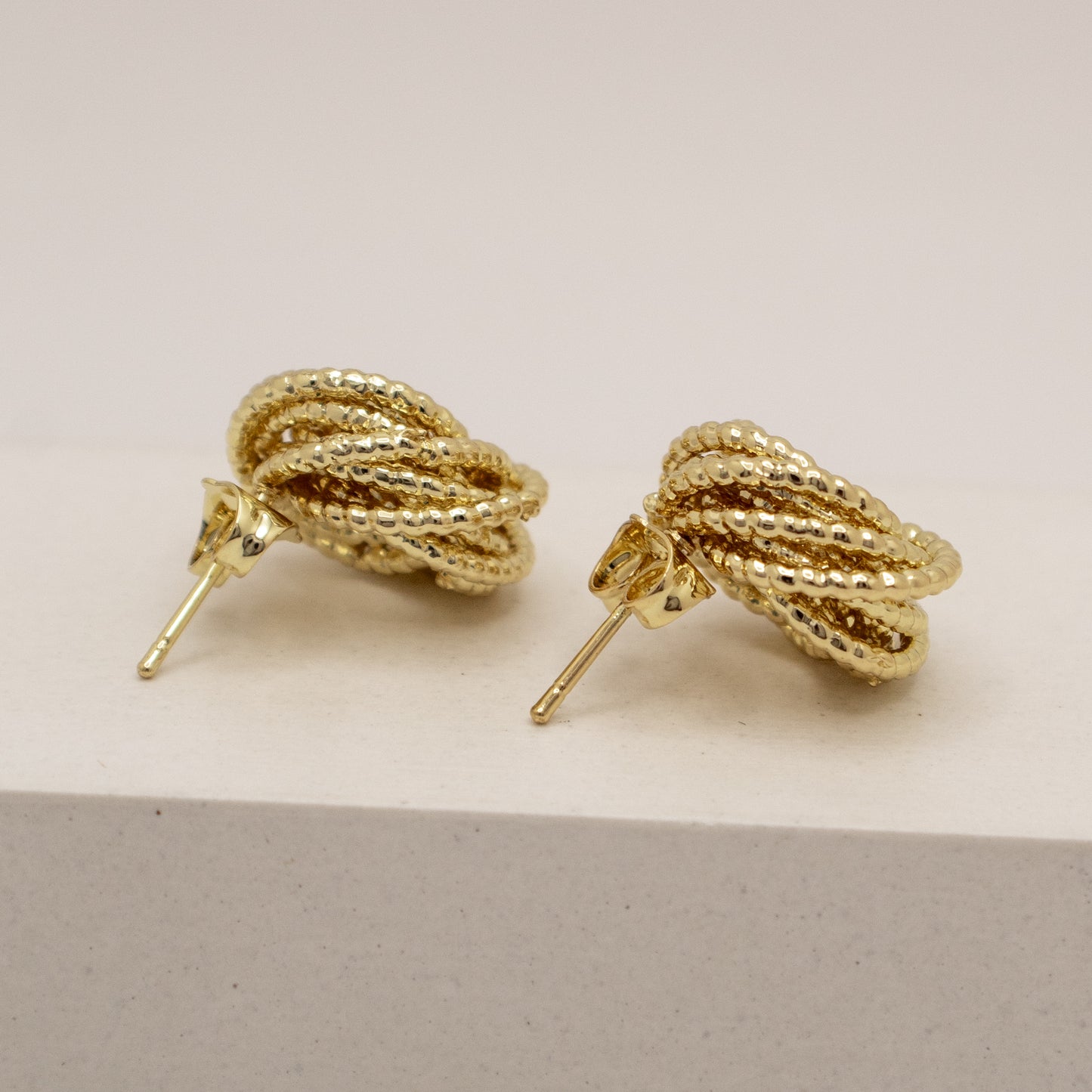 Gold rope-style earrings on a light beige background