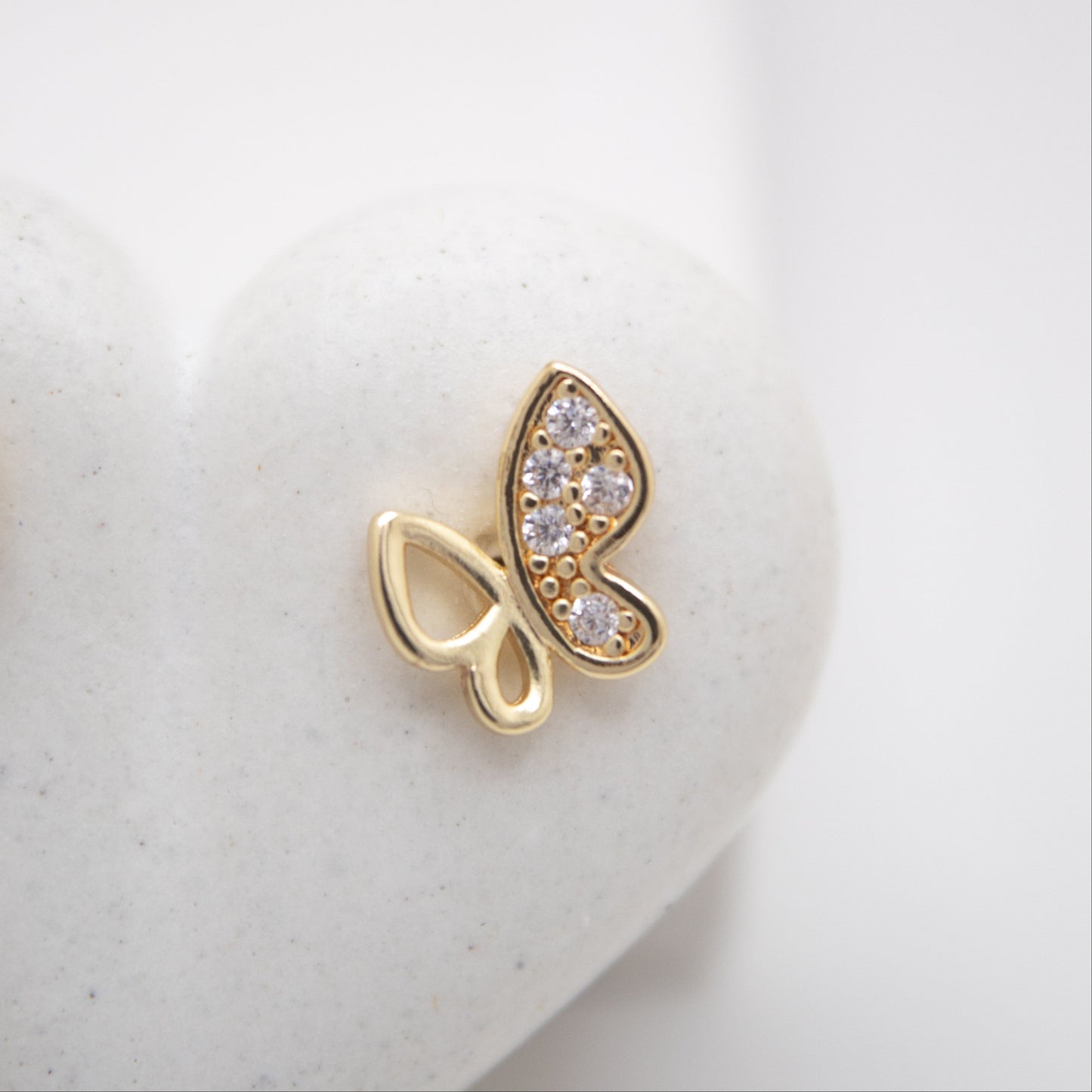Gold butterfly-shaped earring with embedded stones on a white background