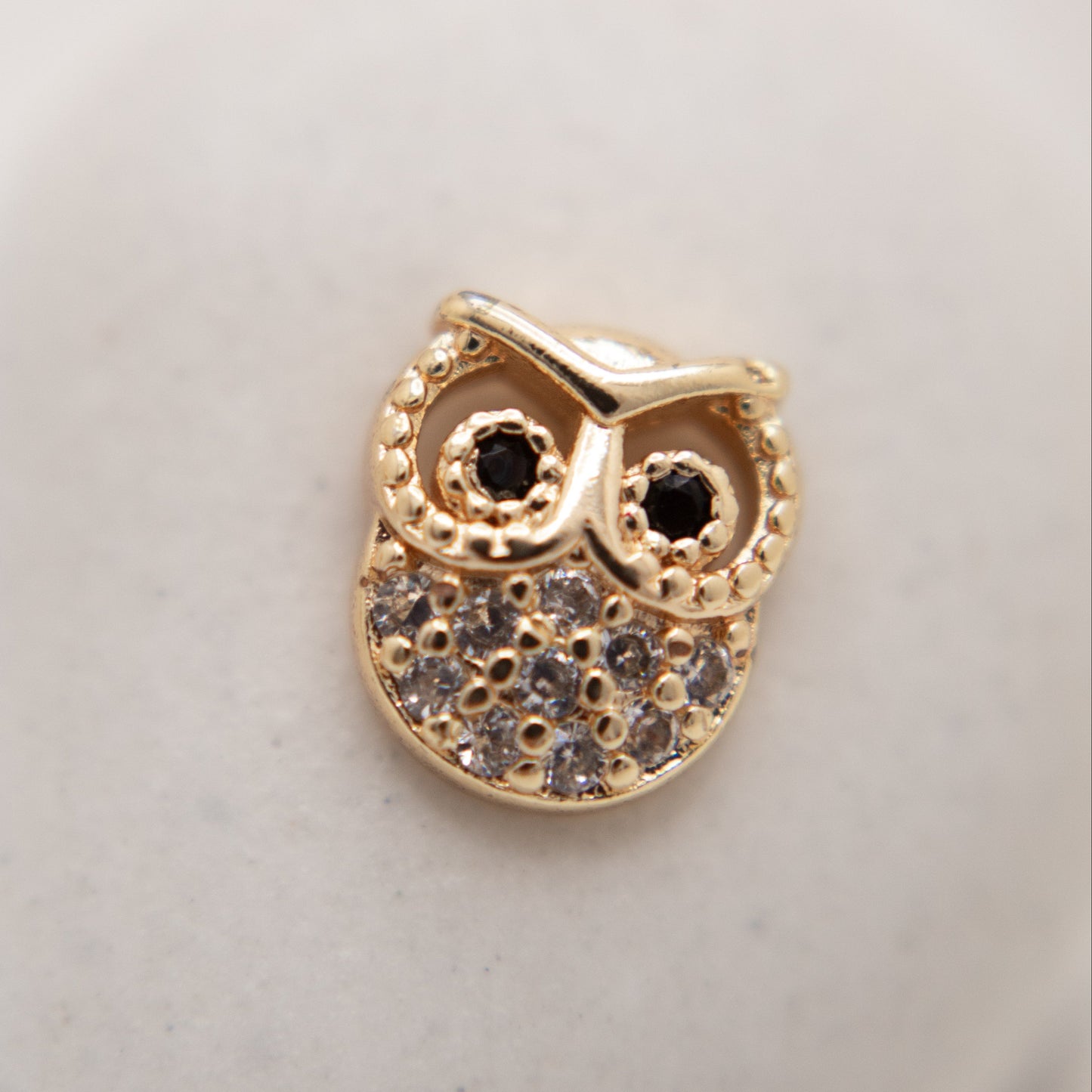 Gold owl-shaped pendant with gemstones on a light background