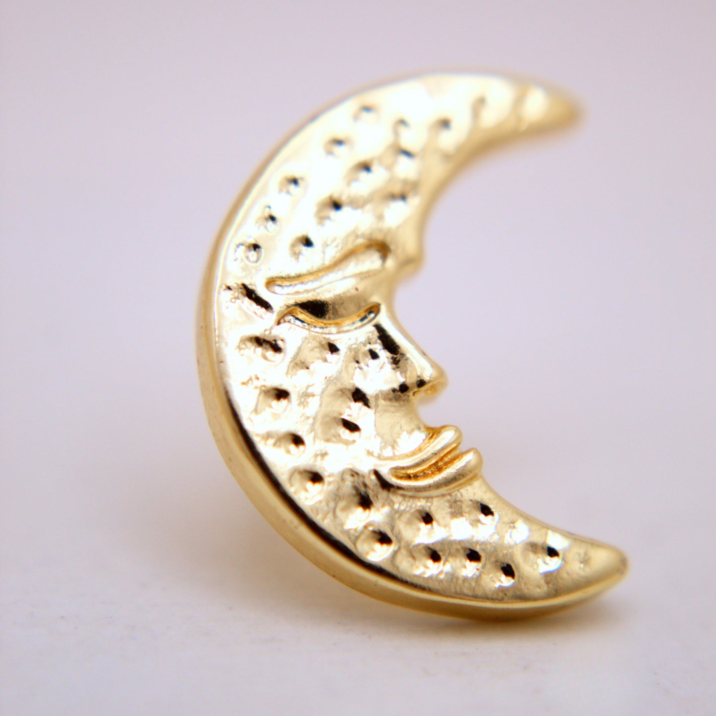 Gold moon-shaped jewelry piece on a light gray background