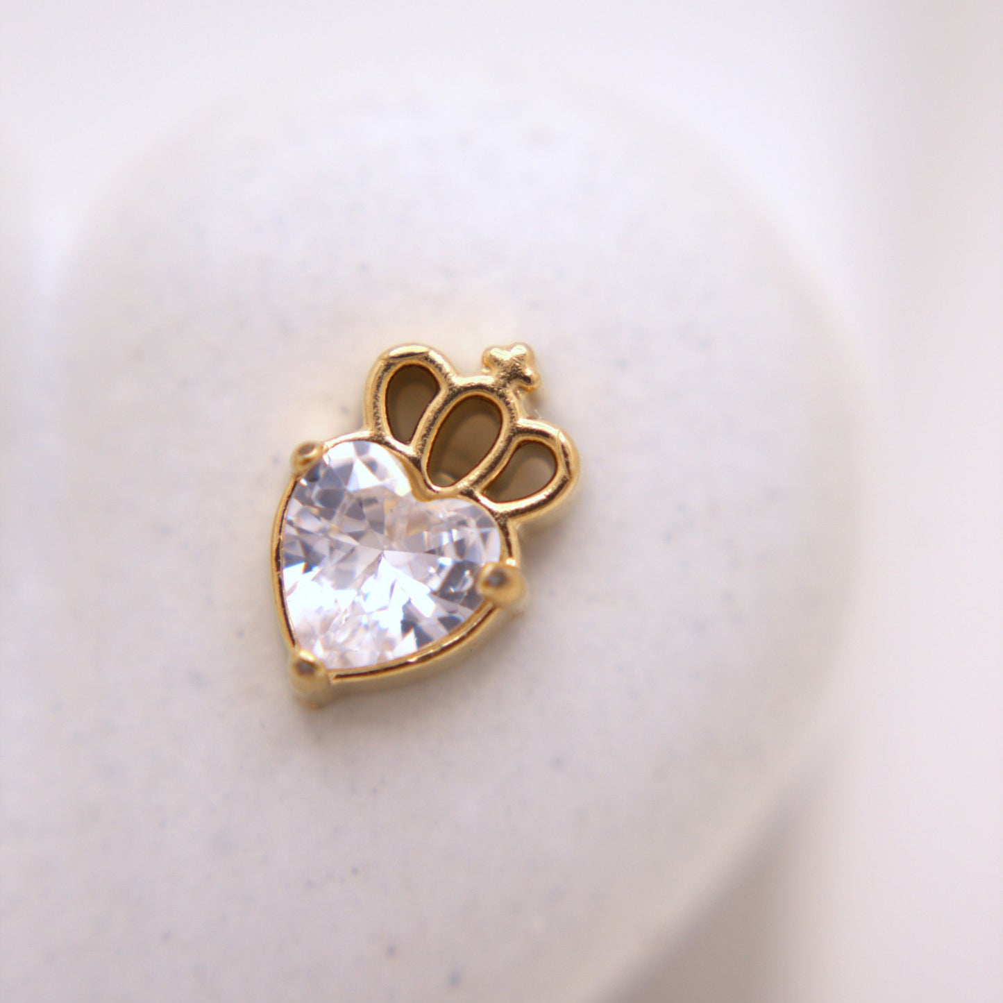 Gold charm with a heart-shaped gem on a light background
