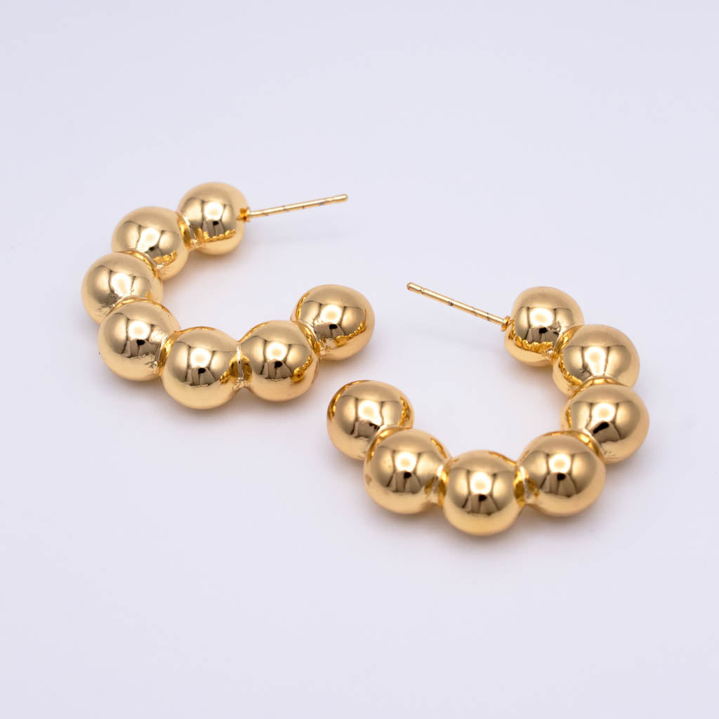 Gold hoop earrings with a segmented, beaded design made of polished spherical links, displayed on a clean white background.