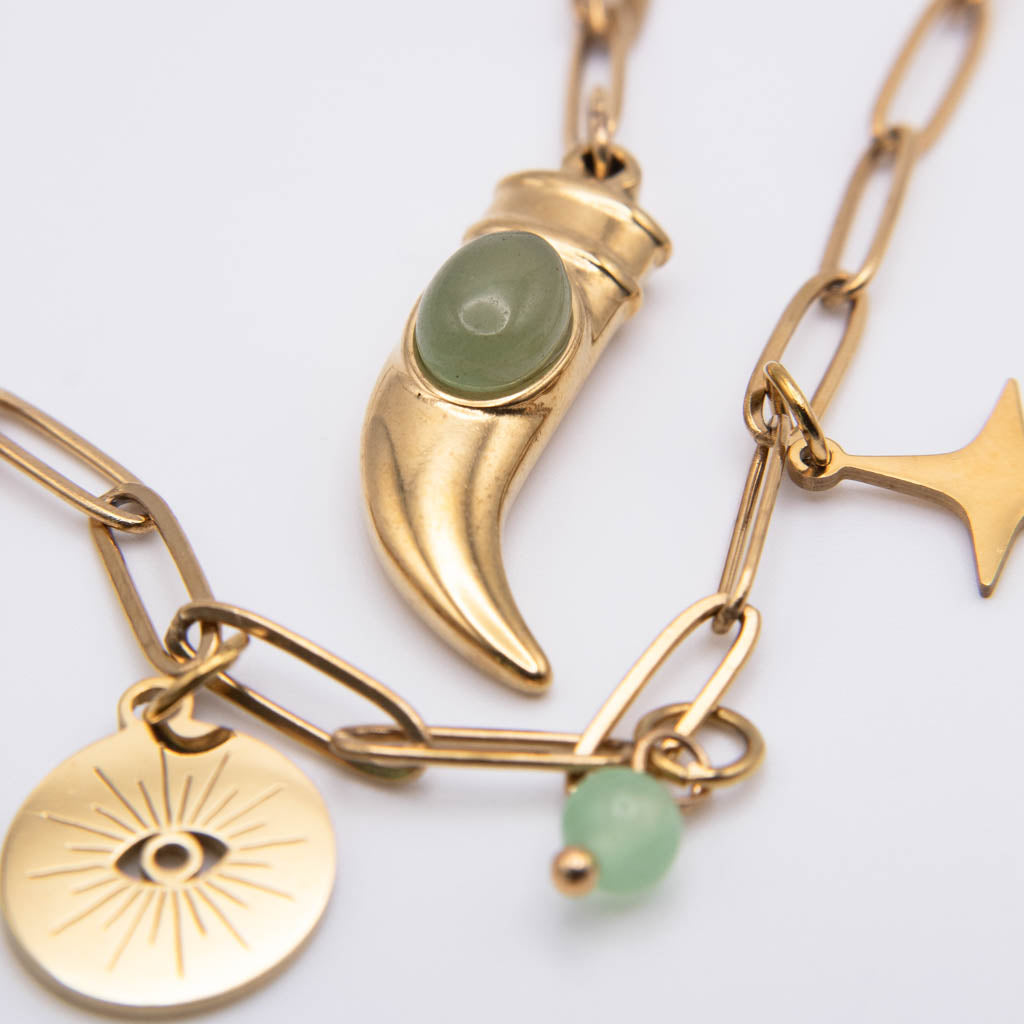 Gold-toned charm necklace featuring a crescent moon pendant with a green stone, a gold disc charm with an eye design, and a small green bead, shown on a white background.