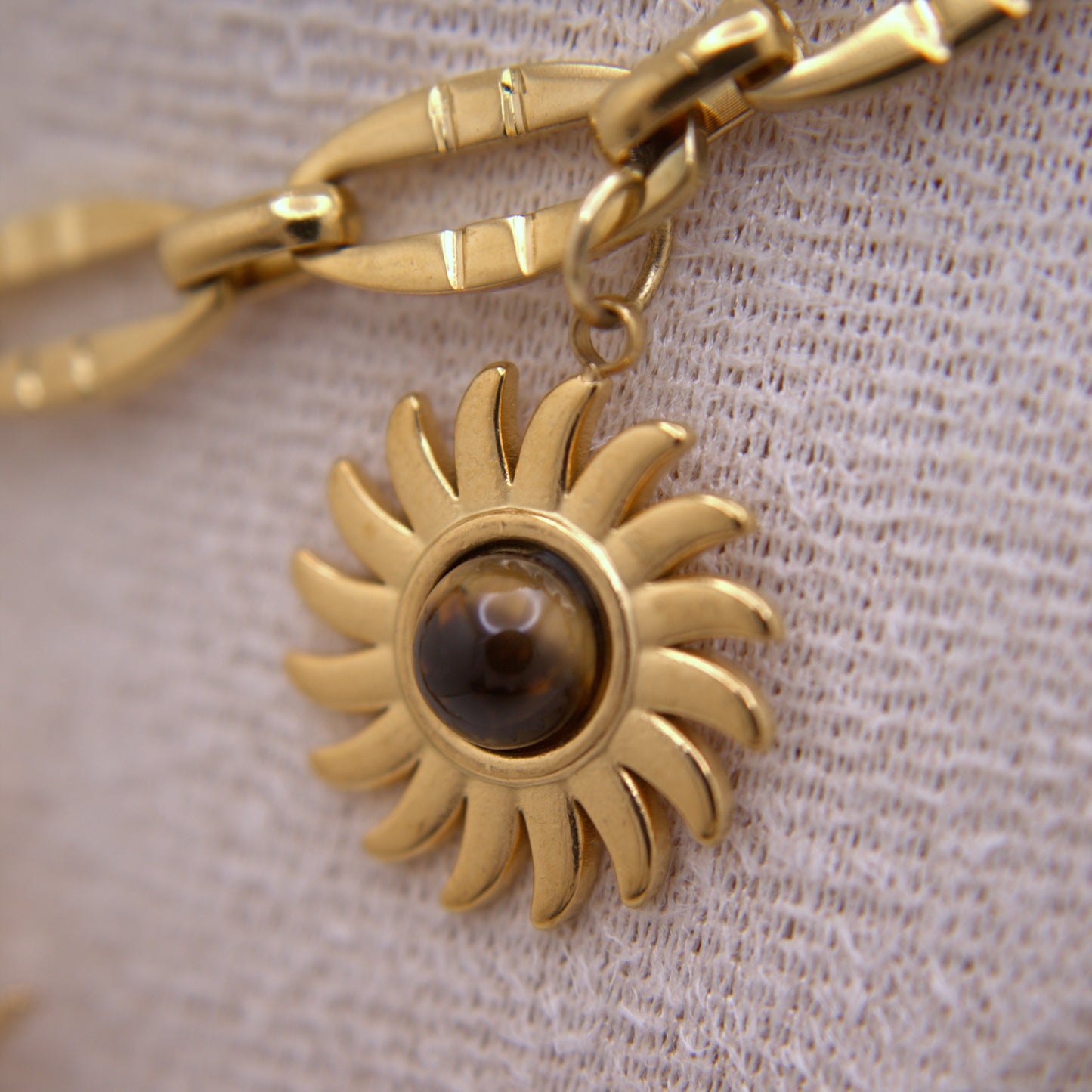 Gold sun-shaped pendant with a central brown gemstone on a beige fabric background