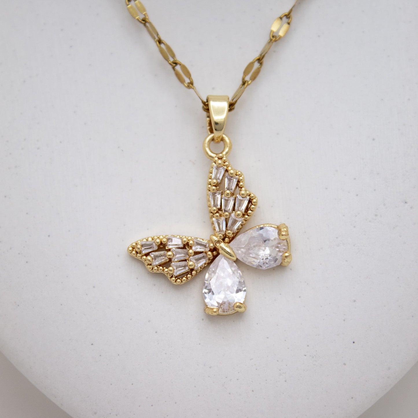 Gold butterfly-shaped pendant necklace on a light gray background
