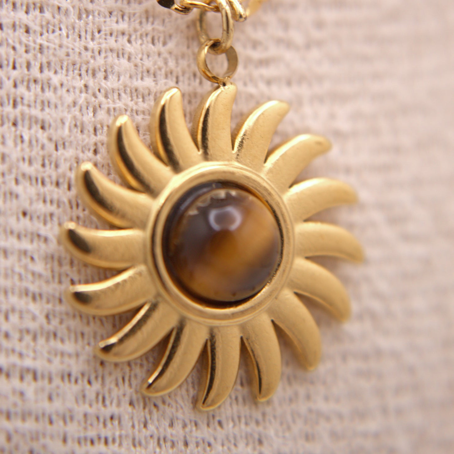 Gold sun-shaped pendant with a central gemstone on a textured beige background