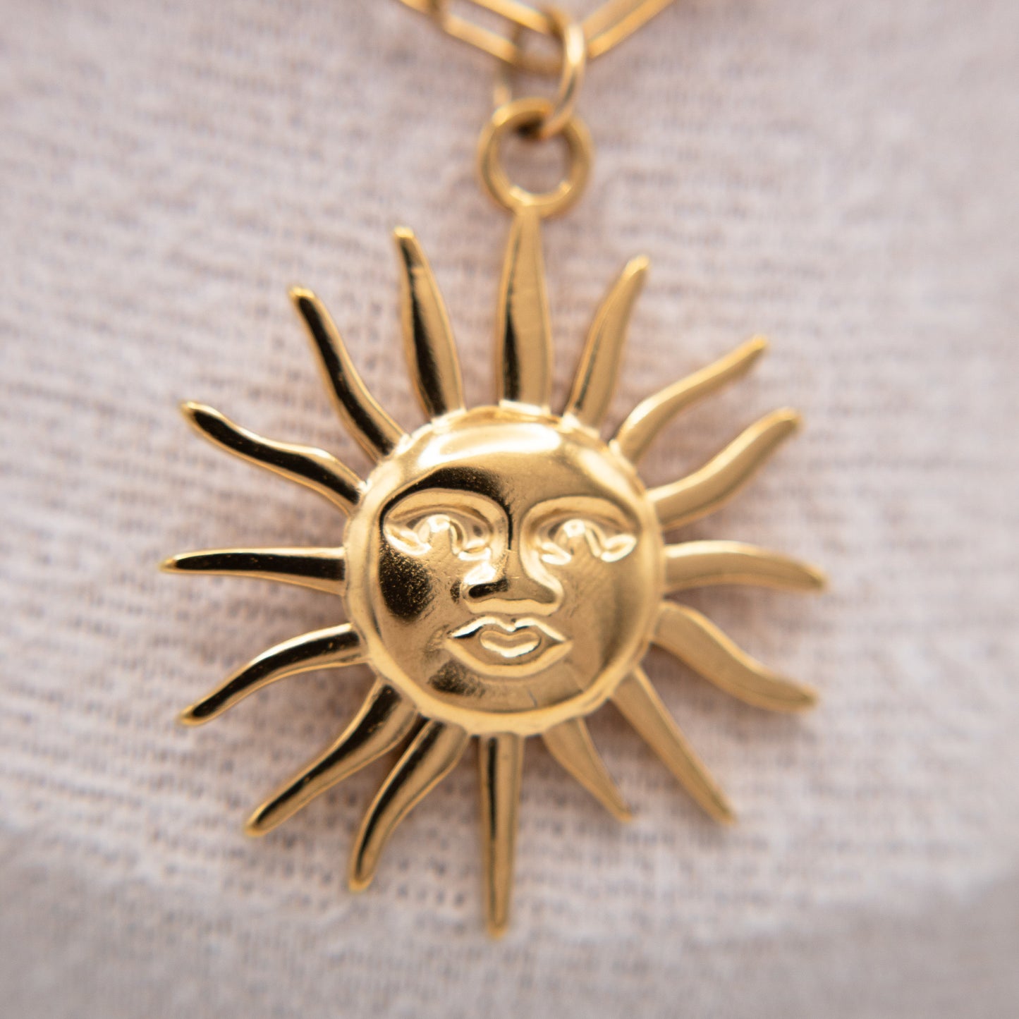 Gold sun-shaped pendant with face on a light fabric background