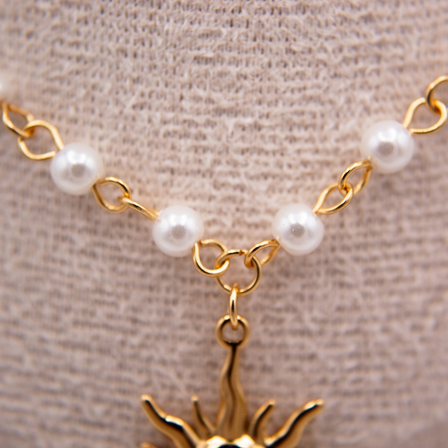 Gold necklace with pearl beads and a sun-shaped pendant on a beige background