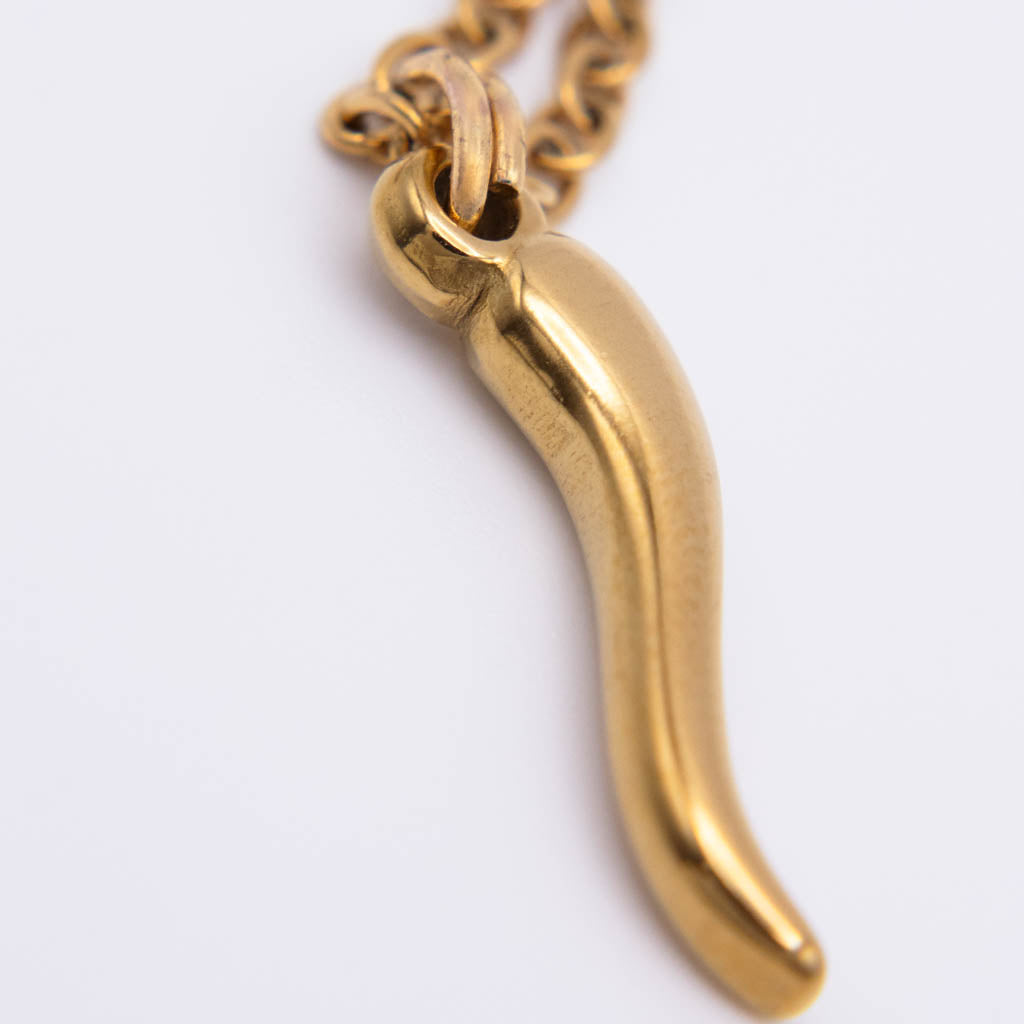 A close-up of a gold-tone pendant necklace shaped like a curved, tapered object, hanging from a matching chain against a plain light background.