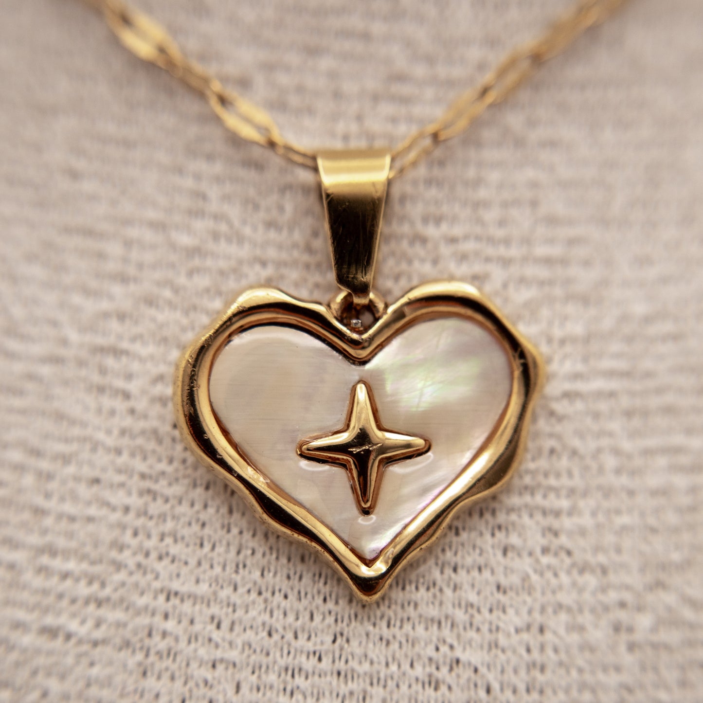 Heart-shaped pendant with star design on a gold chain against a neutral background