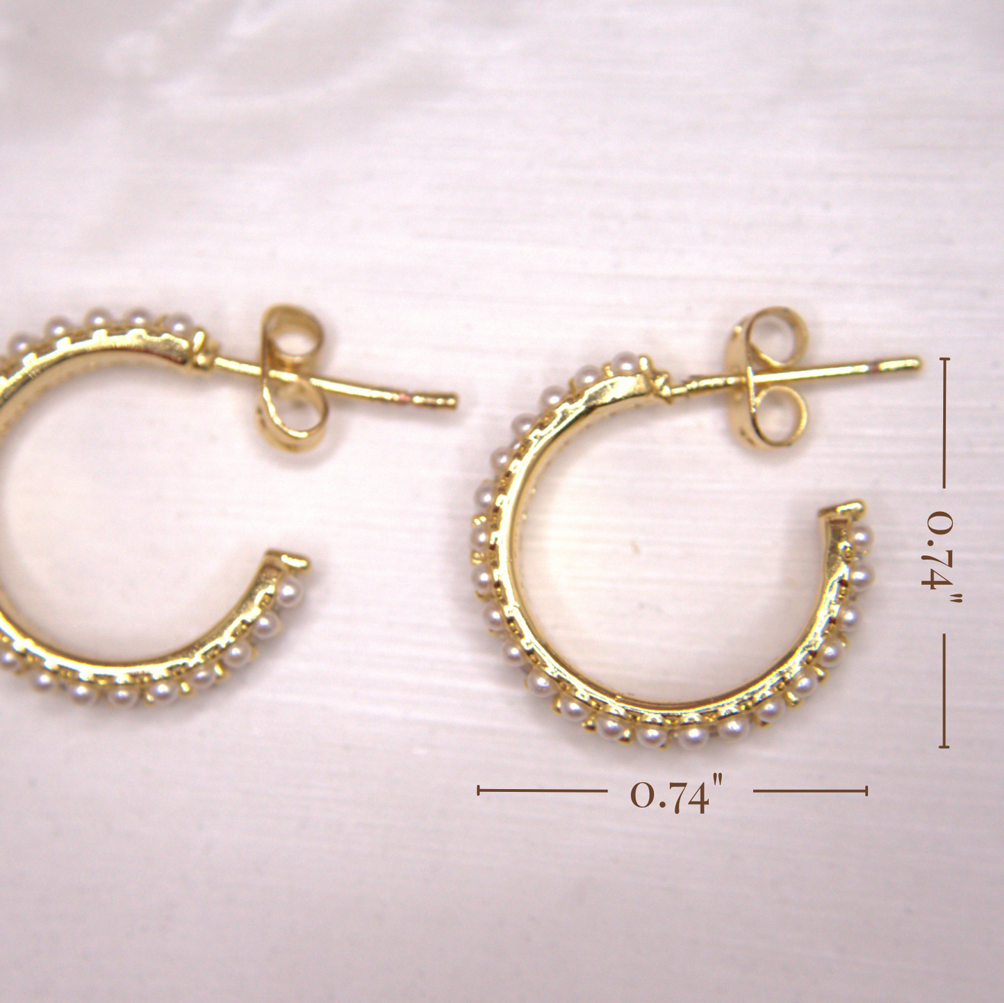 Gold hoop earrings with pearl-like beads on a light pink background