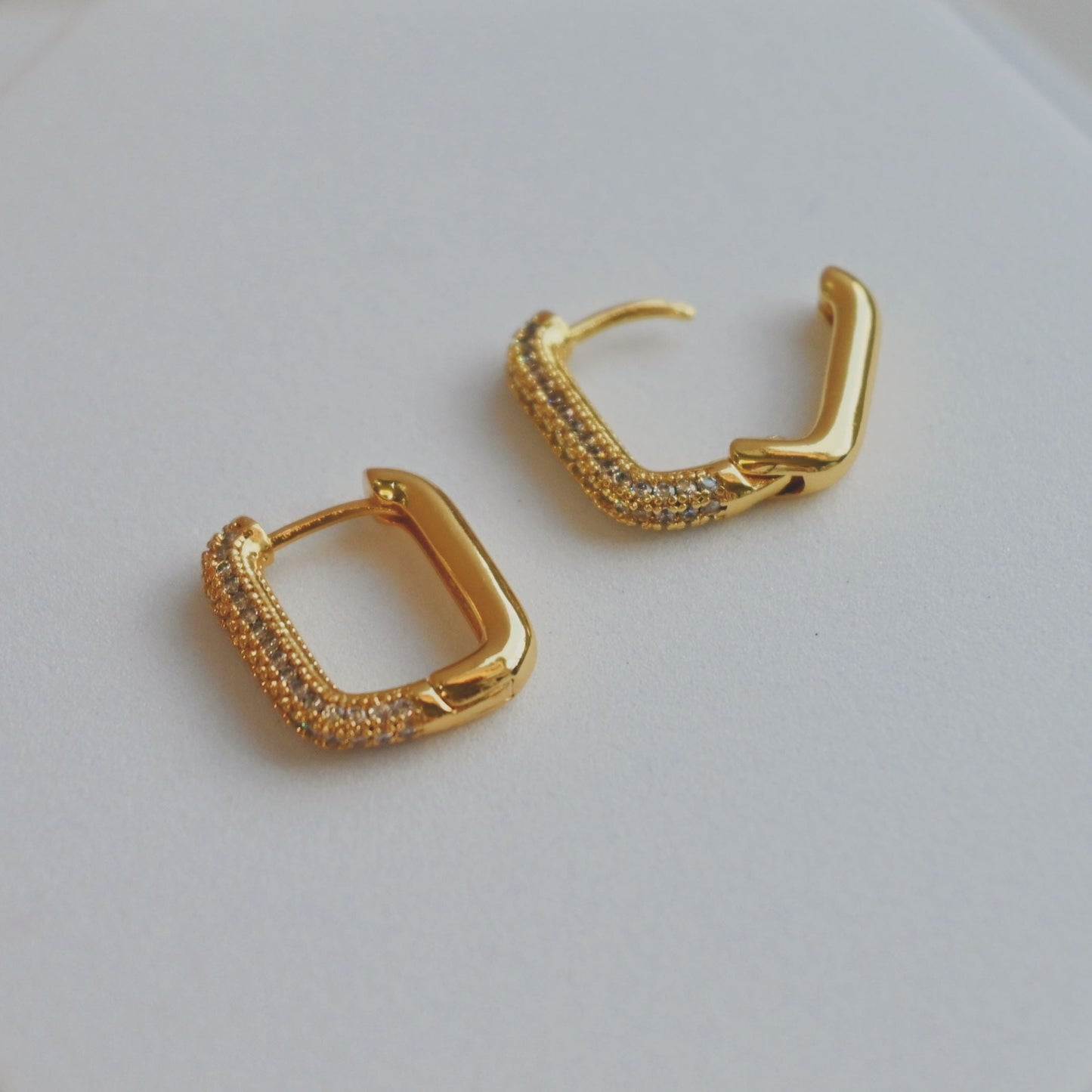 Gold hoop earrings on a white hexagonal stand with a neutral background
