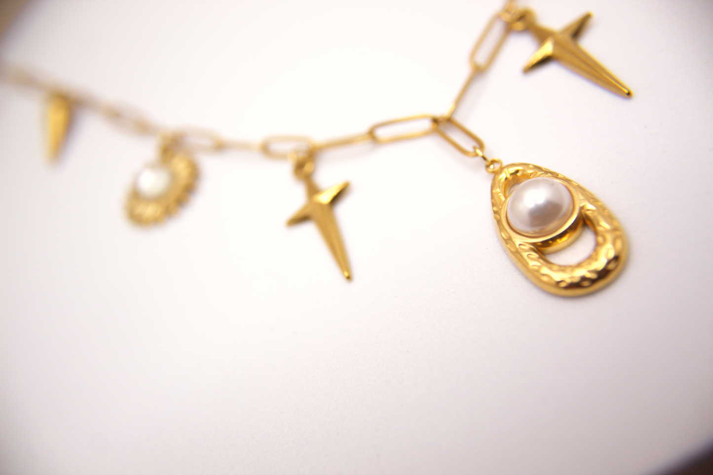 Gold charm necklace with stainless steel chain, pearl and sun details.
