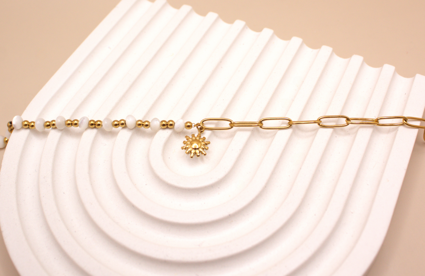 Gold bracelet with white beads, golden chain, and small sun charm.