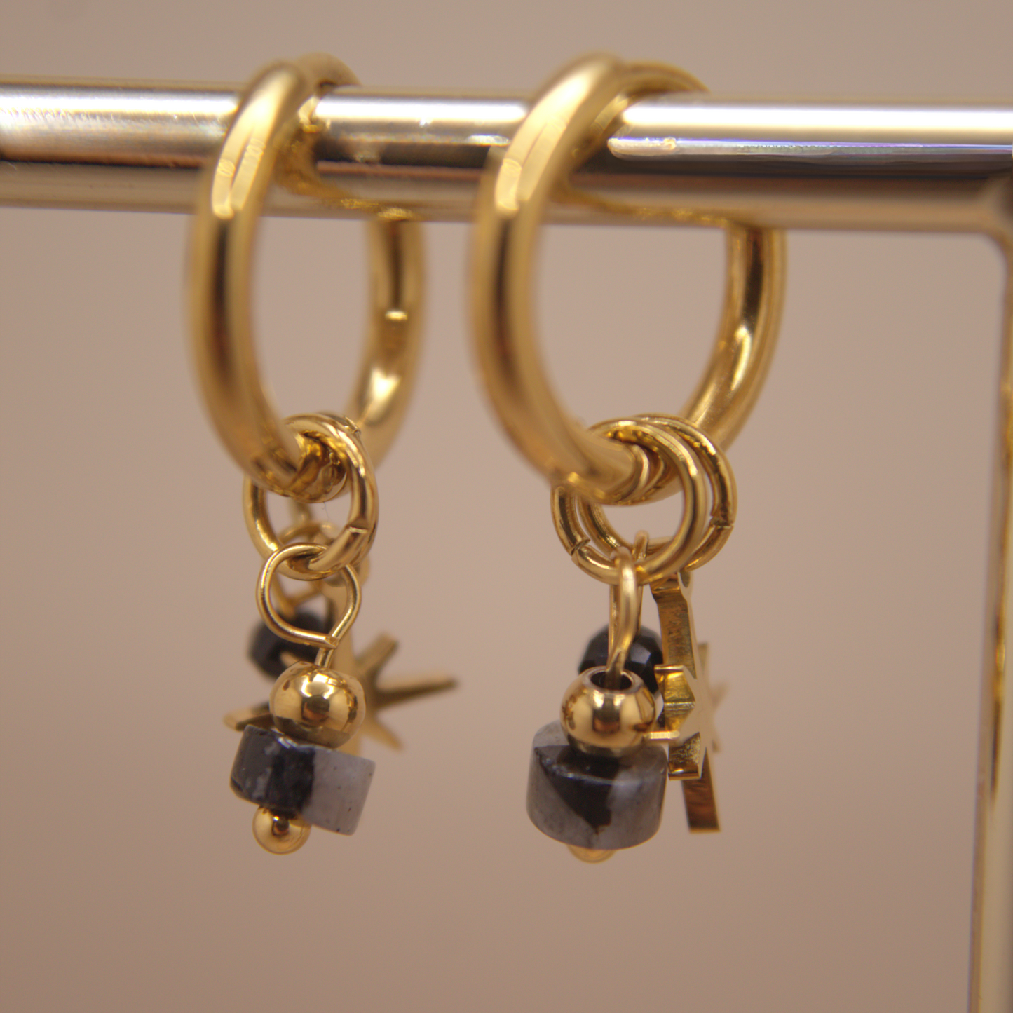 Gold hoop earrings with black beads on a metallic stand.