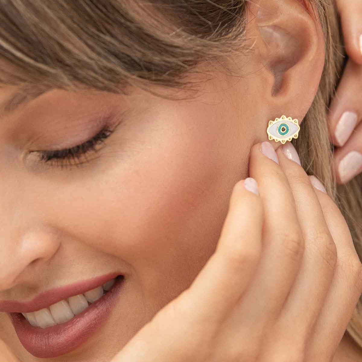 Woman wearing a gold earring with a blue gemstone, close-up of ear and hand.