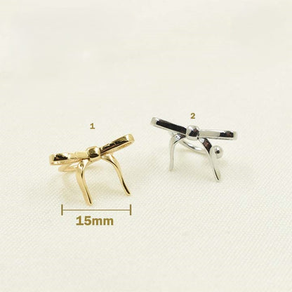 Two ear cuffs, one plated in gold and the other in silver, both designed as bows, displayed against a white background with a measurement scale.