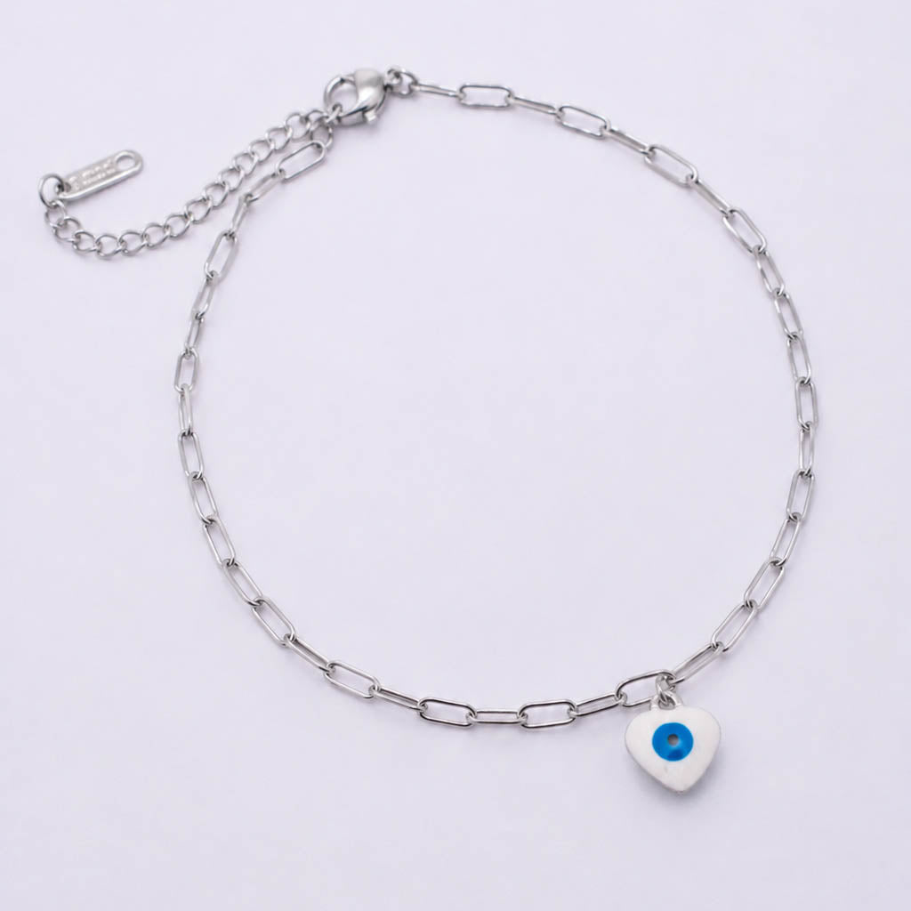 A silver paperclip chain anklet with a small white heart charm featuring a blue evil eye design, displayed on a clean white background.