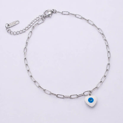 A silver paperclip chain anklet with a small white heart charm featuring a blue evil eye design, displayed on a clean white background.