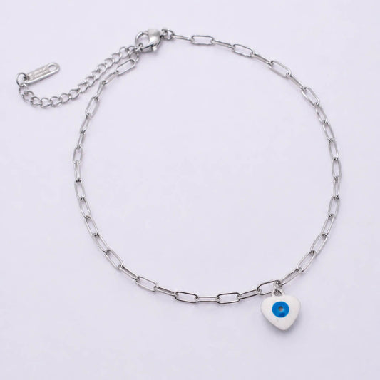 A silver paperclip chain anklet with a small white heart charm featuring a blue evil eye design, displayed on a clean white background.