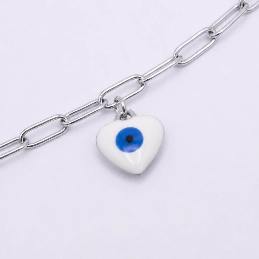 A silver paperclip chain anklet featuring a white ceramic evil eye heart charm with a blue and black eye design, shown on a light gray background.