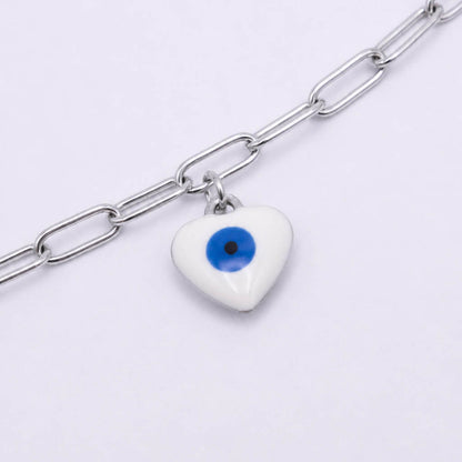 A silver paperclip chain anklet featuring a white ceramic evil eye heart charm with a blue and black eye design, shown on a light gray background.
