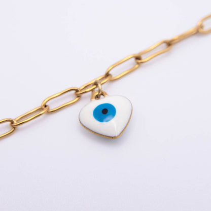 A gold paperclip chain anklet featuring a small white enamel evil eye charm with a blue iris and black pupil, set against a plain white background.