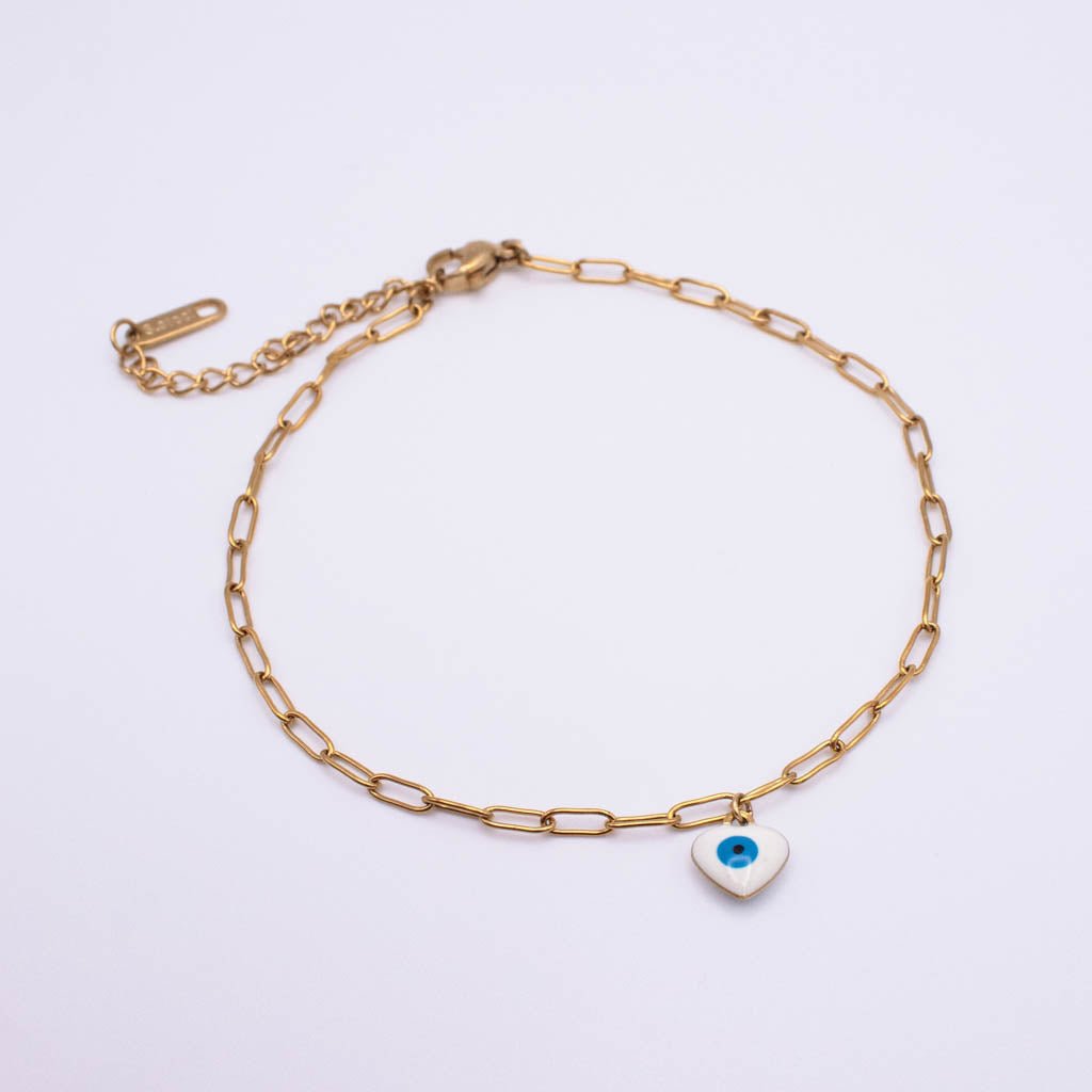 A gold paperclip chain anklet with an adjustable lobster clasp and extender chain, featuring a small white heart charm with a blue and black evil eye design, displayed on a clean white background.