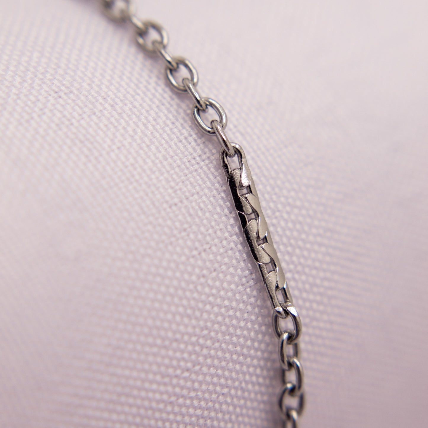 Close-up of a silver chain bracelet anklet on a light pink fabric background
