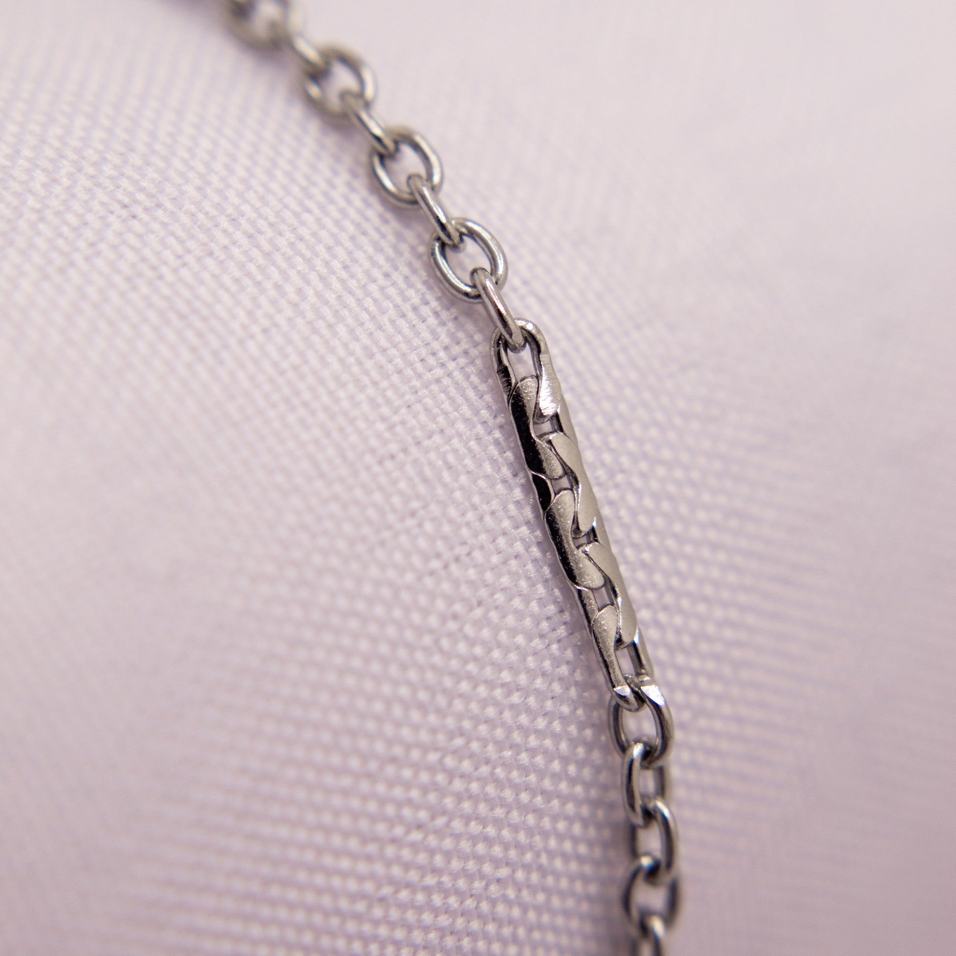 Close-up of a silver chain bracelet anklet on a light pink fabric background