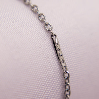 Close-up of a silver chain bracelet anklet on a light pink fabric background