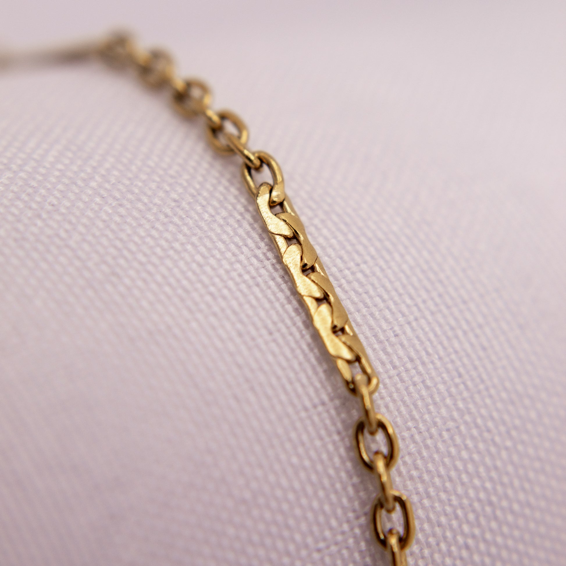 Gold chain bracelet anklet on a light pink textured background